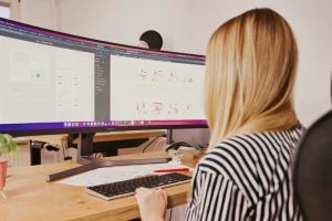 aswebdesign Kobieta siedząca przy biurku z dwoma monitorami przed sobą, pracująca na Stronach internetowych.
